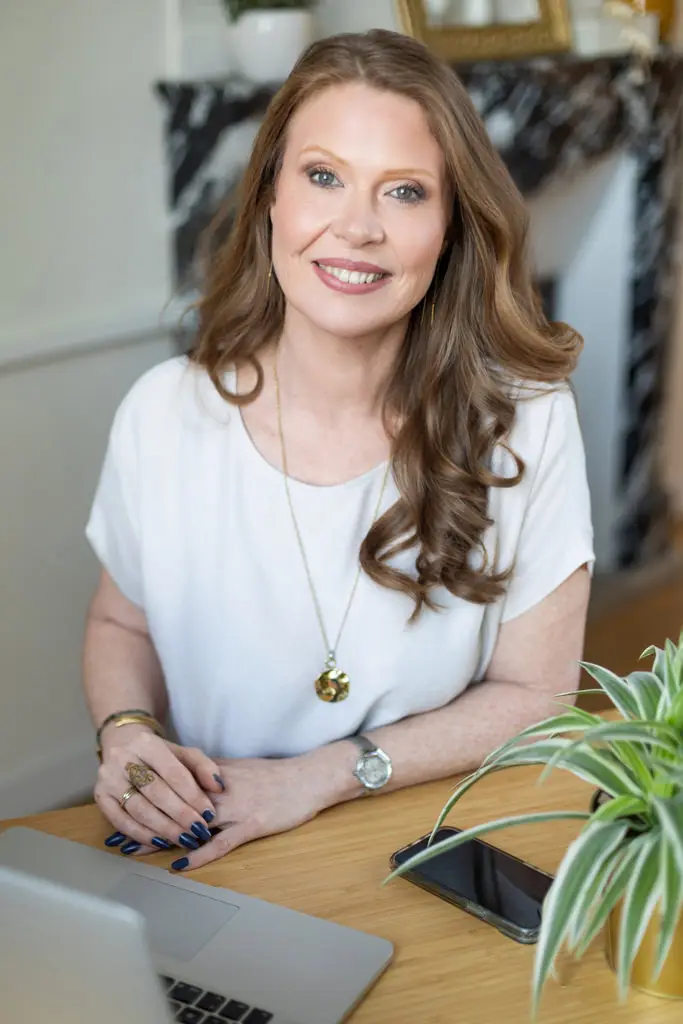 Portrait professionnel de Sandra Delannoy, accompagnante de thérapeutes, assise à son bureau avec un sourire chaleureux, devant un ordinateur portable.